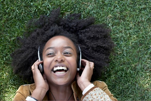 Woman with headphones lying on grass laughing